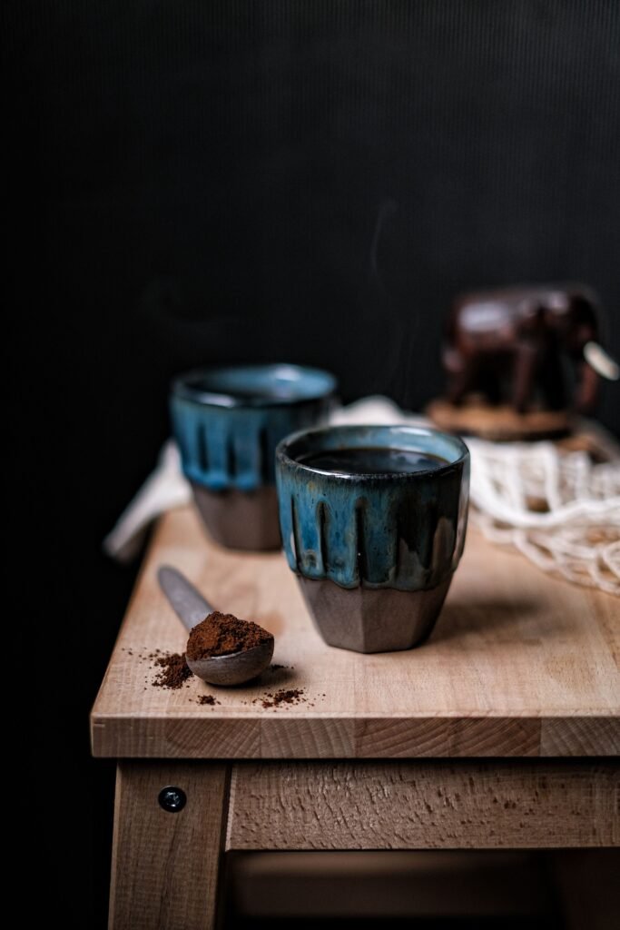 木板上的兩只藍褐色陶杯、黑咖啡與盛咖啡粉的木匙