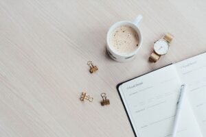 淺色木桌上的卡布奇諾、金色手錶與翻開的目標筆記本