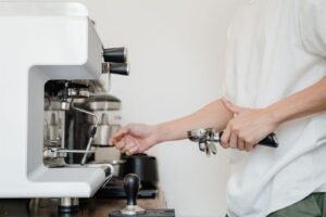 一人一手握著沖煮把手、一手操作白色義式咖啡機，呈現獨立操作咖啡機的練習情境