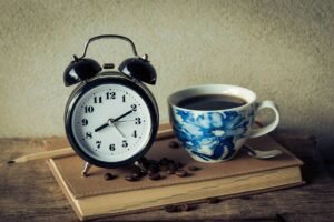 鬧鐘、藍色花紋咖啡杯與咖啡豆擺在筆記本上，呈現時間安排與補課規劃的概念