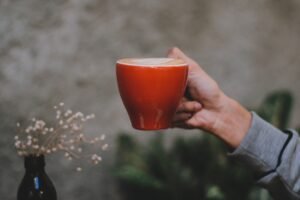 一隻手拿著紅色咖啡杯,杯面有拿鐵拉花,背景有乾燥小花,紅色帶出節慶氣氛